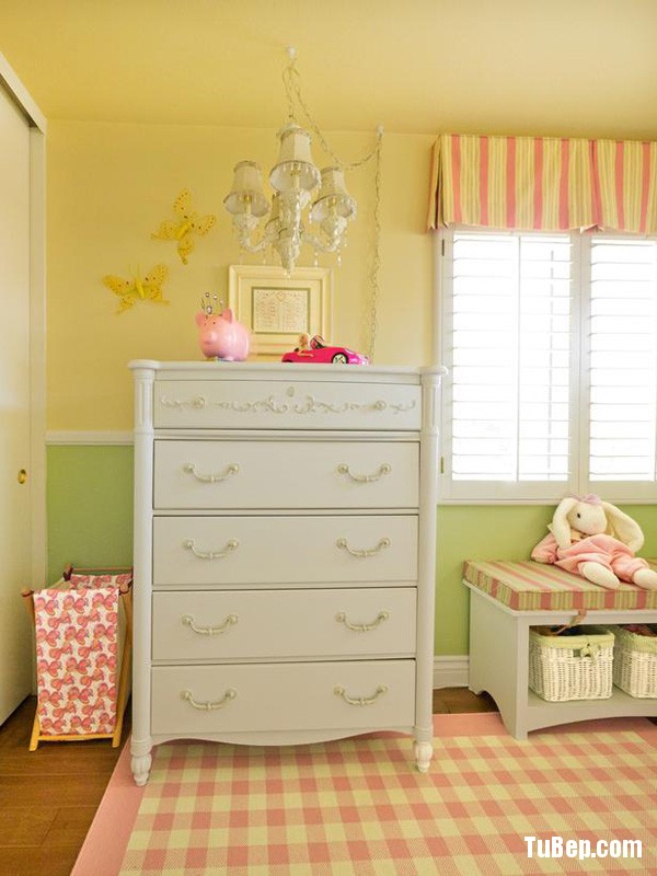 A tall dressser with a chandelier with decorative crystals, checkered rug, storage bench fill this little girls room with design and color.