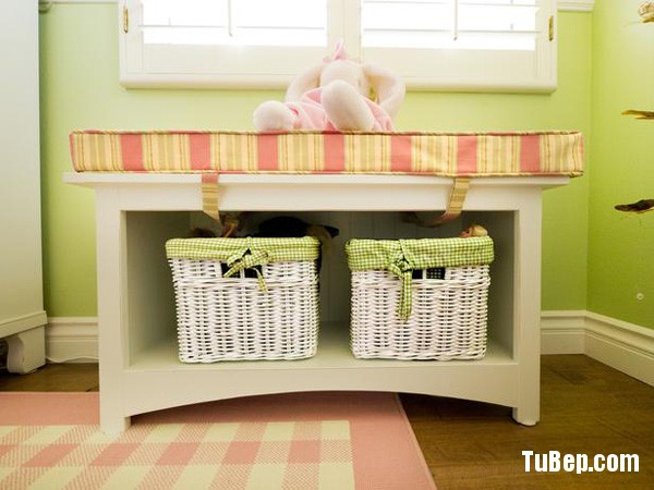 Girls bedroom storage bench with wicker baskets for storing kids toys and items and a seating area with stuffed animal. This area has a pink checkered rug on the floor under the window.