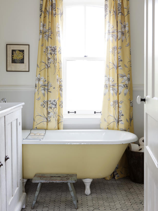 Yellow and white bathroom design with floral curtains, above ground tub with claw feet, stool, and white vanity.